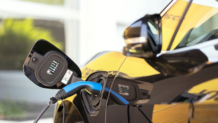 Electric car with plug-in socket at charge station charging battery