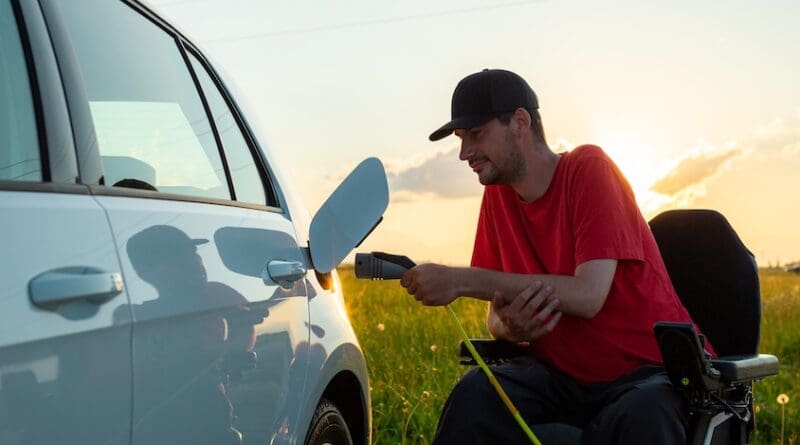 Man in wheelchair plugging in a charger in an electric car
