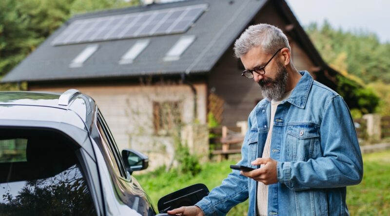 man charging his EV in front of a house with solar panels